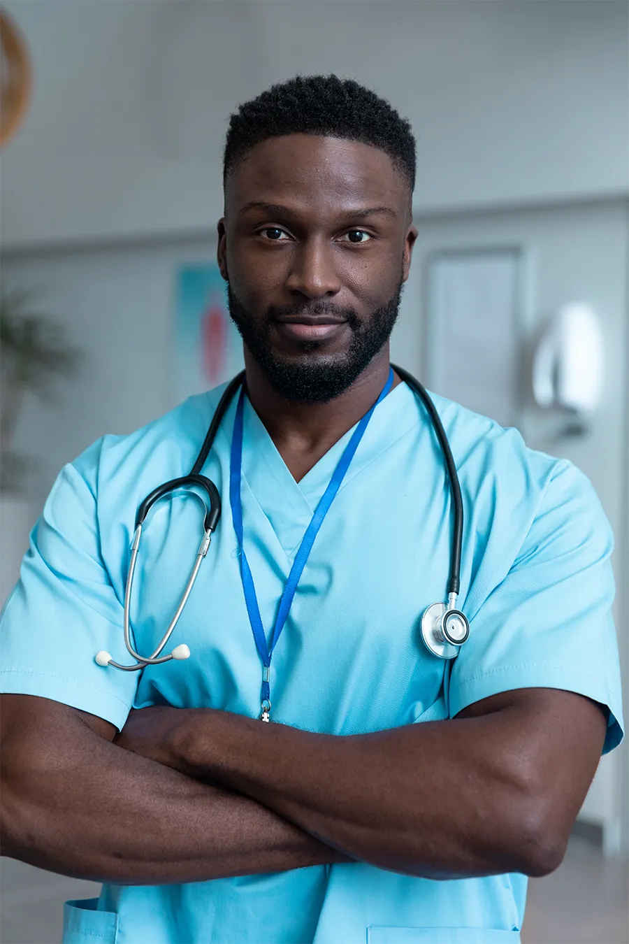 Black doctor wearing blue scrubs with his arms crossed