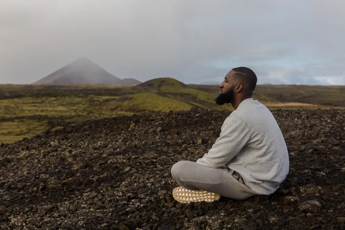 Black man seated outdoors looking toward distant mountains