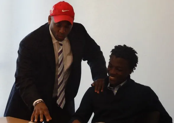 Two Black men in conversation, one seated and one leaning forward