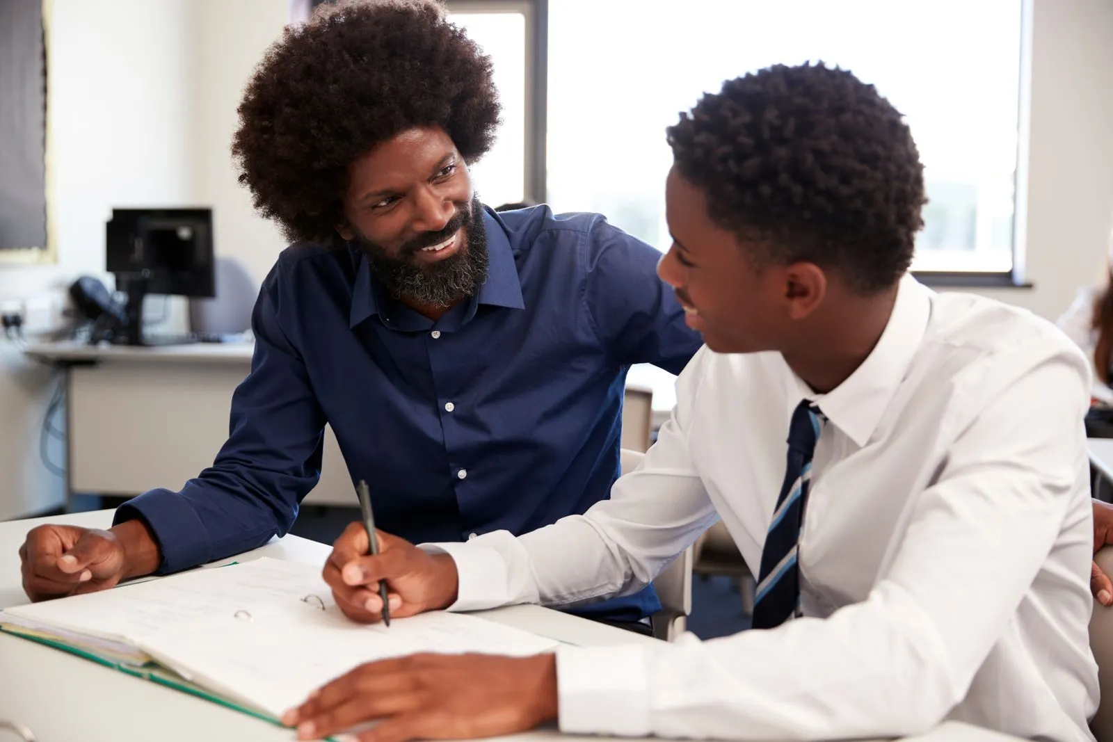 Two Black men reviewing a notebook at a desk