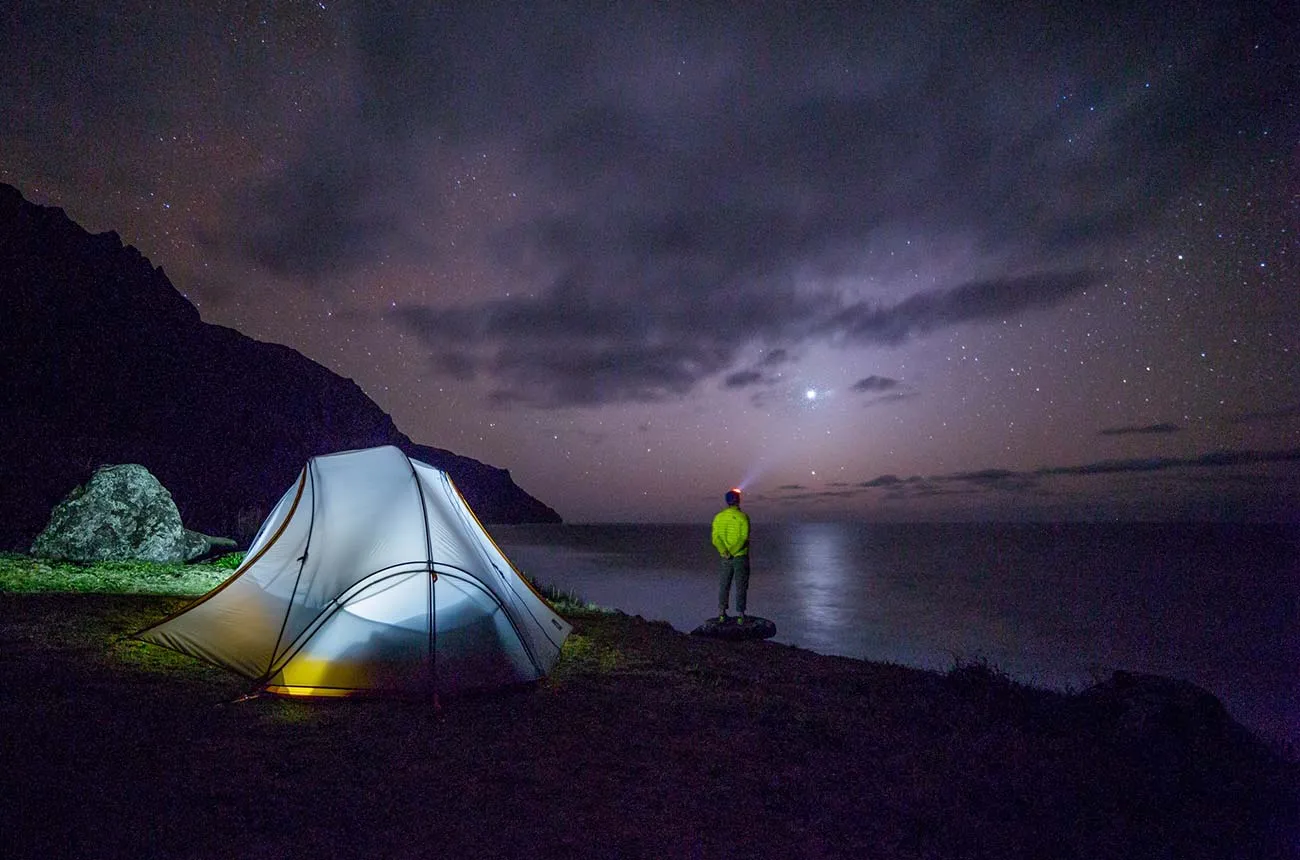Illuminated tent beside mountains under a night sky