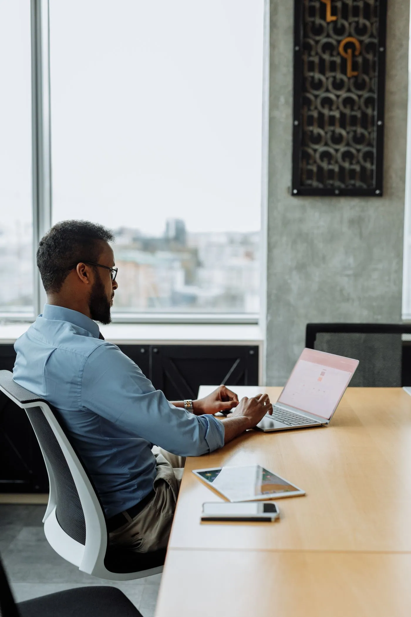 Black man working on a laptop beside a window overlooking the city